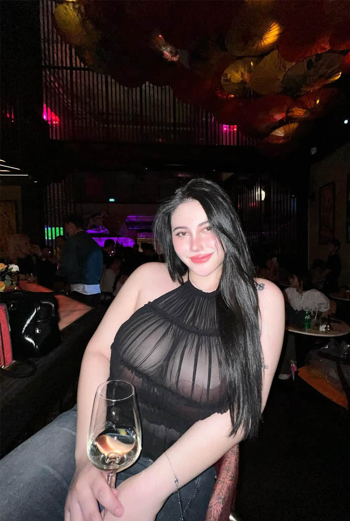 Avnika Sexy Escort enjoying a classy dinner night, wearing a sheer black top and holding a wine glass in a luxury restaurant ambiance.