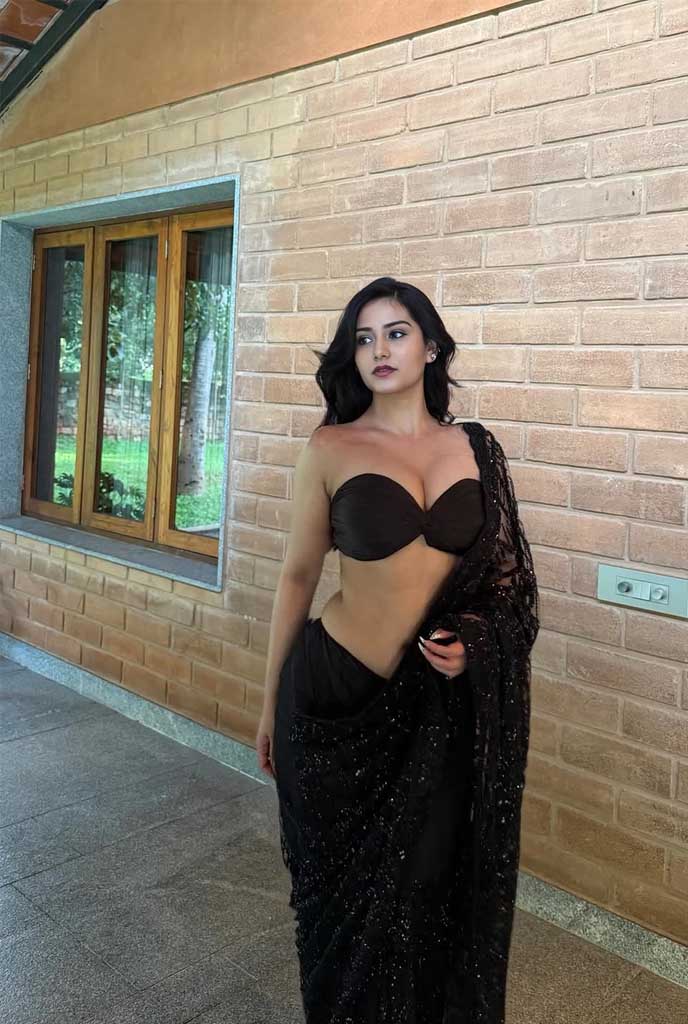 Anika Hot Escort posing in a stylish black saree outfit near a window in Siliguri, showcasing elegance and bold charm.